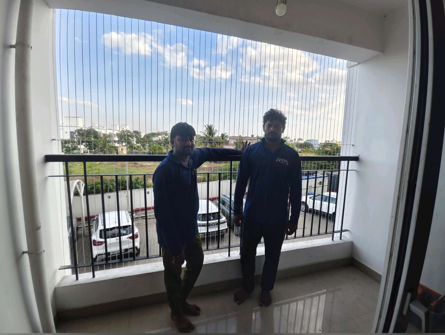 Two installers fitting cables across a wide balcony opening — real YPL work shown for Kovur customers