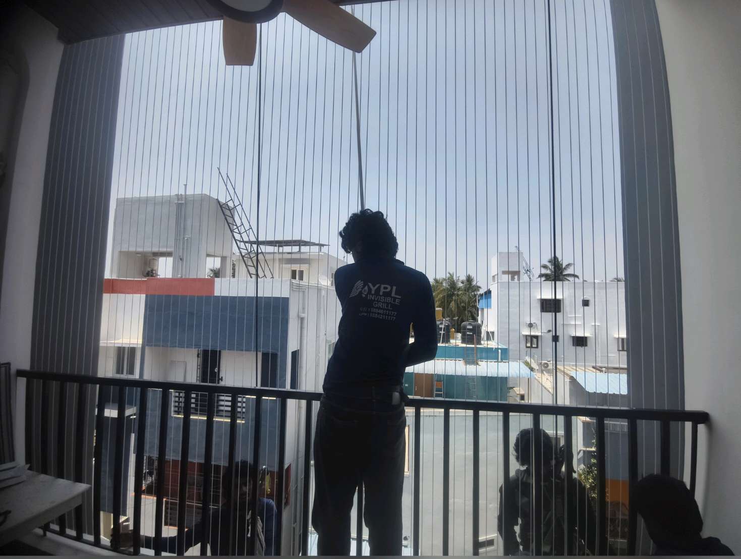 Installer at work behind balcony grill cables — real YPL work shown for Karambakkam customers